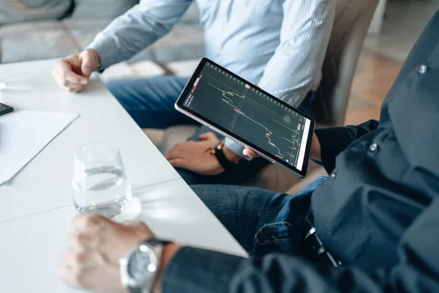 Two businessmen analyzing stock market data on a tablet in a modern office setting. A method for business software buyer personas that record authority, not personality