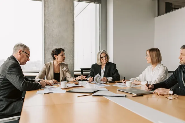 Five business professionals engaged in a meeting in a modern office setting, discussing documents and ideas. Business productivity software skills forecast: a scenario